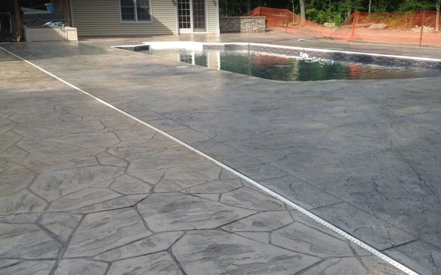 Stamped concrete patio with a pool, house, and trees. Gray stone-like pattern.