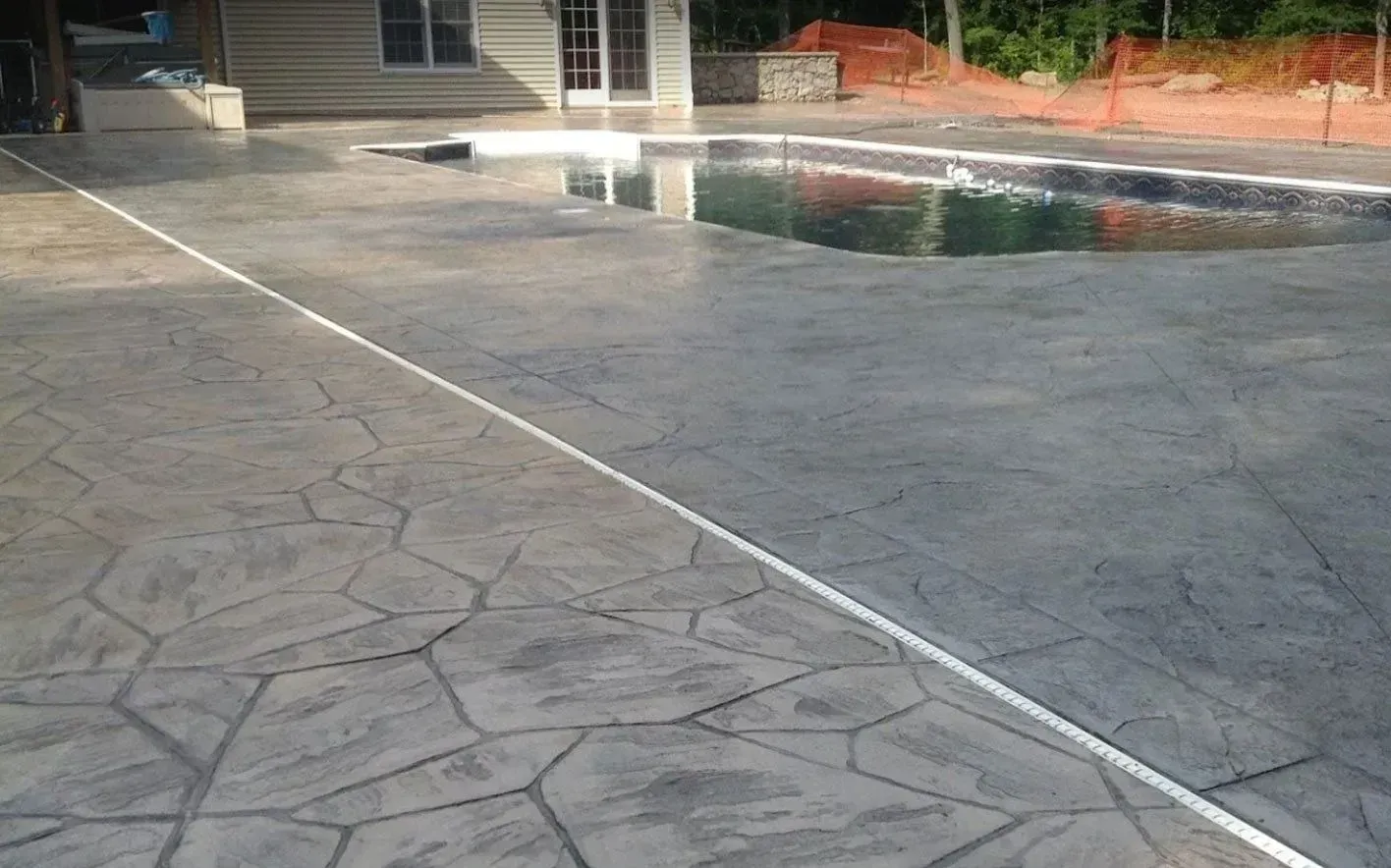 Stamped concrete patio with a pool in the background, featuring a stone pattern and a white dividing line.