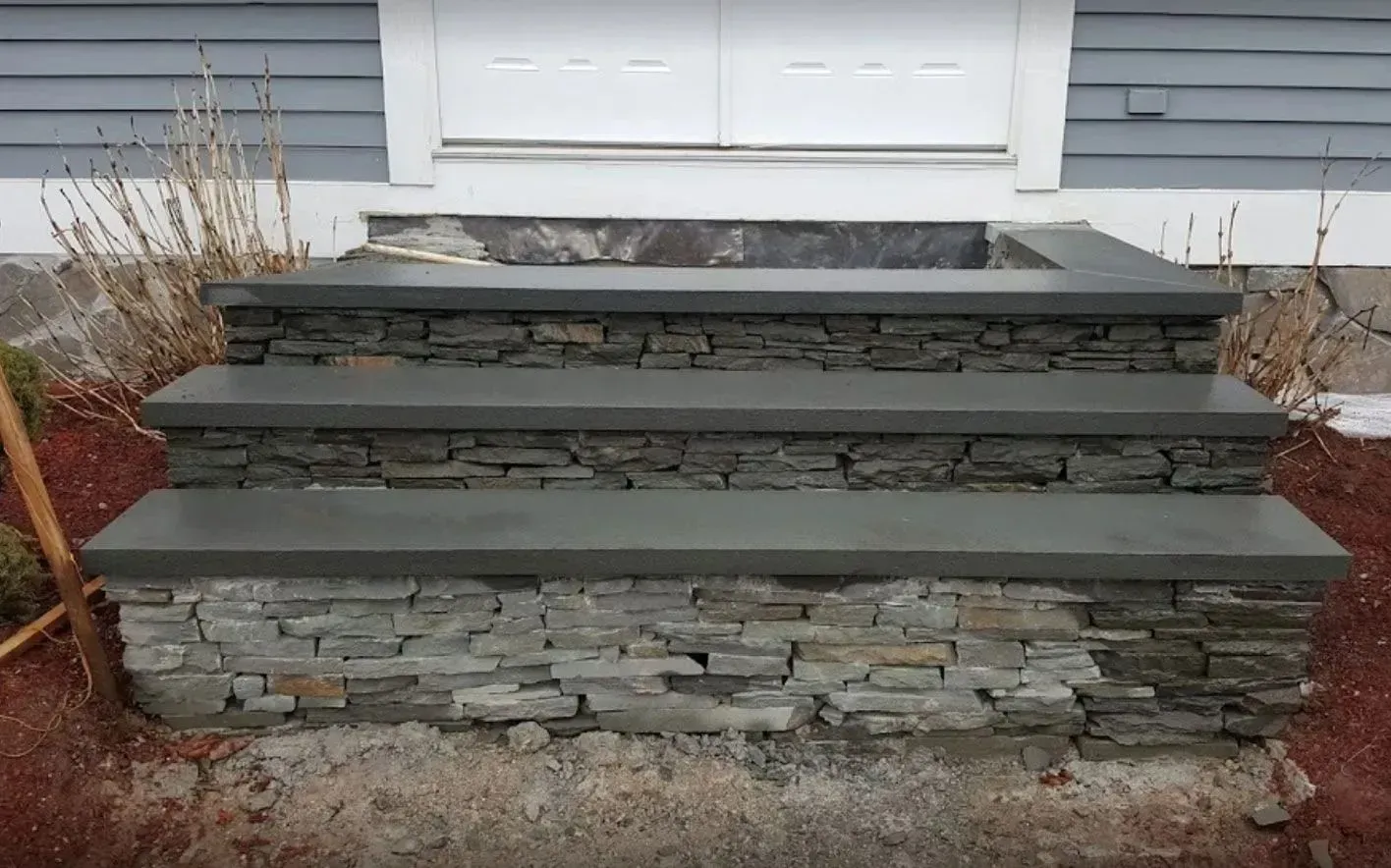 Stone steps leading to a white door, with a stone facade and dark gray treads.