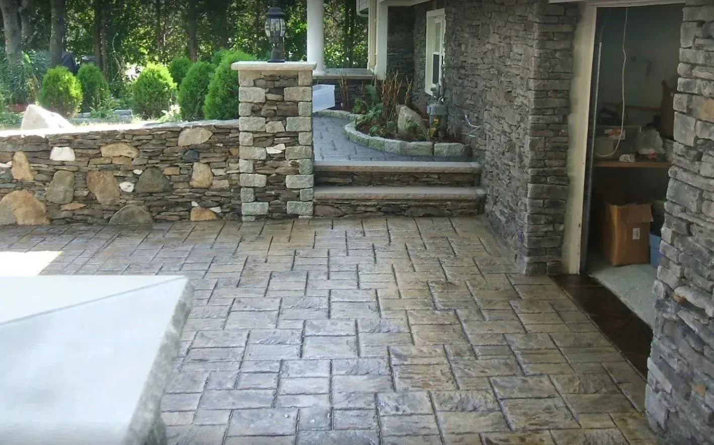 Stone patio with stamped brick pattern, leading to a home's entrance, featuring stone walls and steps.