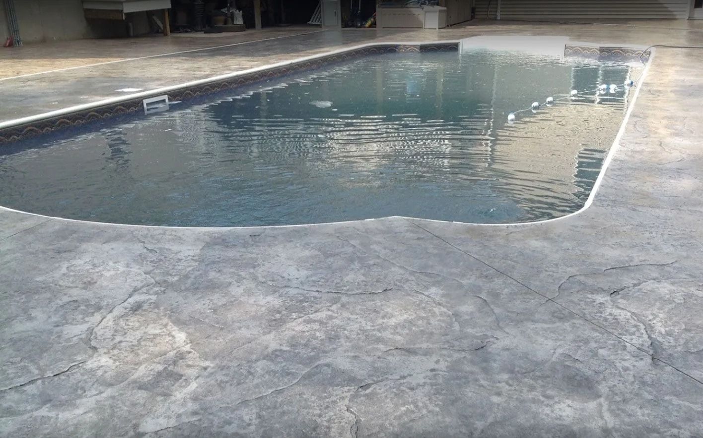 Concrete pool deck surrounds a rectangular pool filled with water.