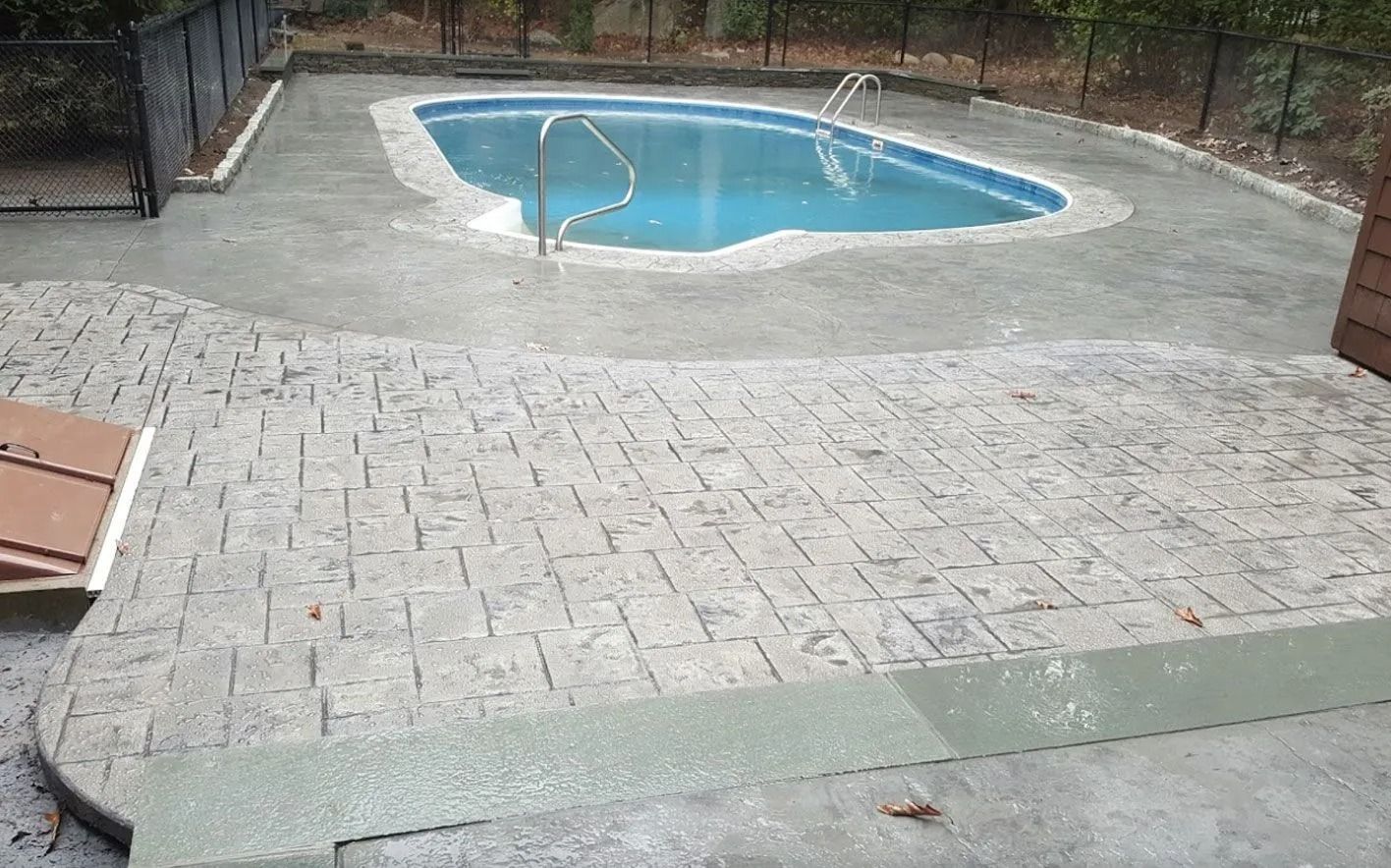 Concrete pool deck with stamped brick pattern, leading to a swimming pool.