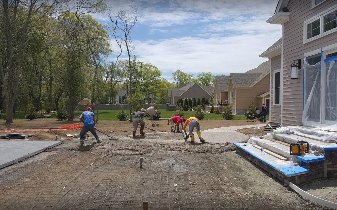 Construction workers pouring concrete patio, residential backyard.