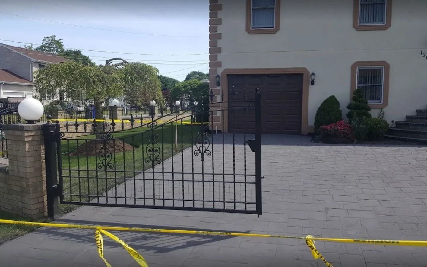 Black gate and driveway lead to a beige house, yellow caution tape, sunny day.