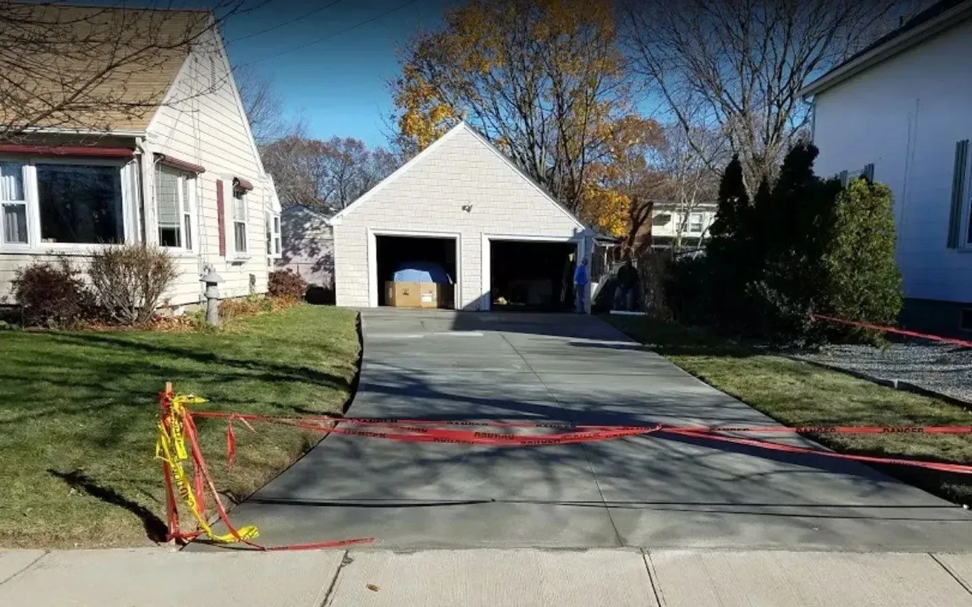 Driveway leading to a two-car garage, flanked by houses under a blue sky, caution tape present.