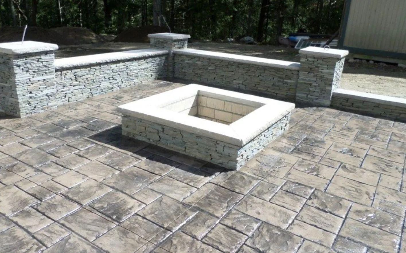 Stone fire pit on a stamped concrete patio, surrounded by stone walls and pillars in an outdoor setting.