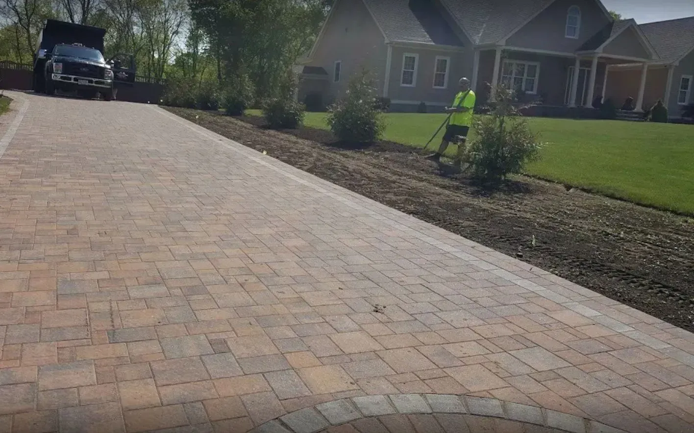 Brick driveway leading to a house, a person working on landscaping, and a truck.