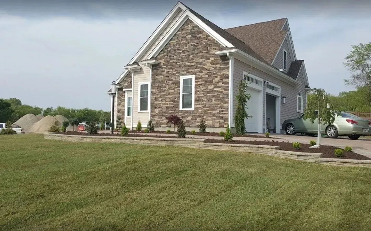 Stone-faced house with two-car garage, manicured lawn, and driveway.