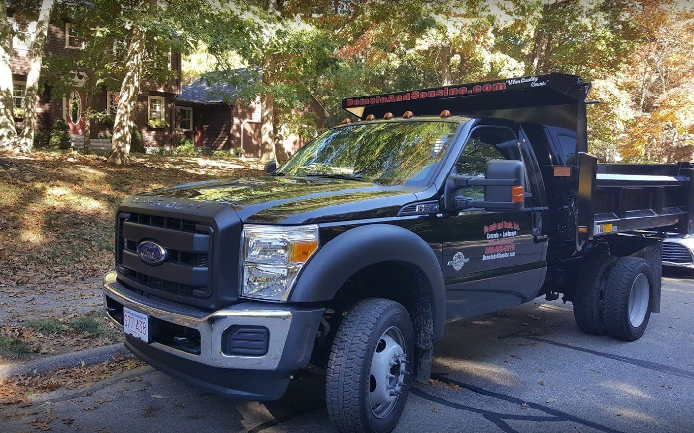 Black Ford dump truck parked on a paved road in front of a residential building on a sunny day.