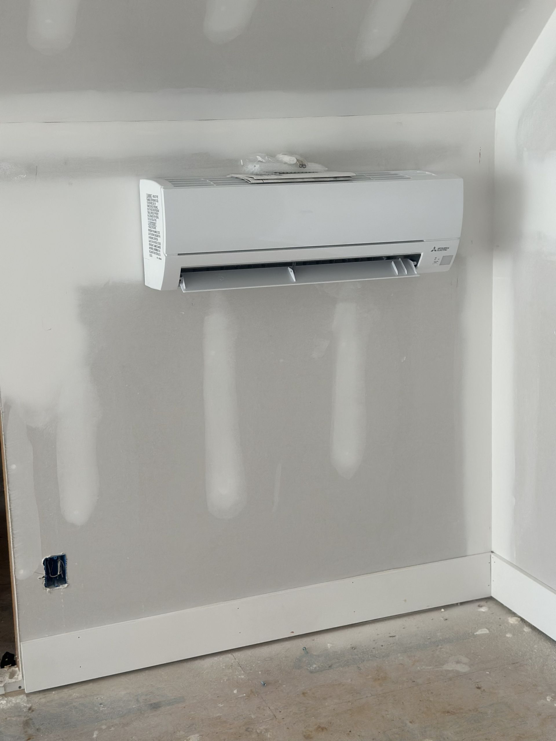 A wall-mounted white air conditioning unit installed on an unfinished drywall wall with visible plaster seams.