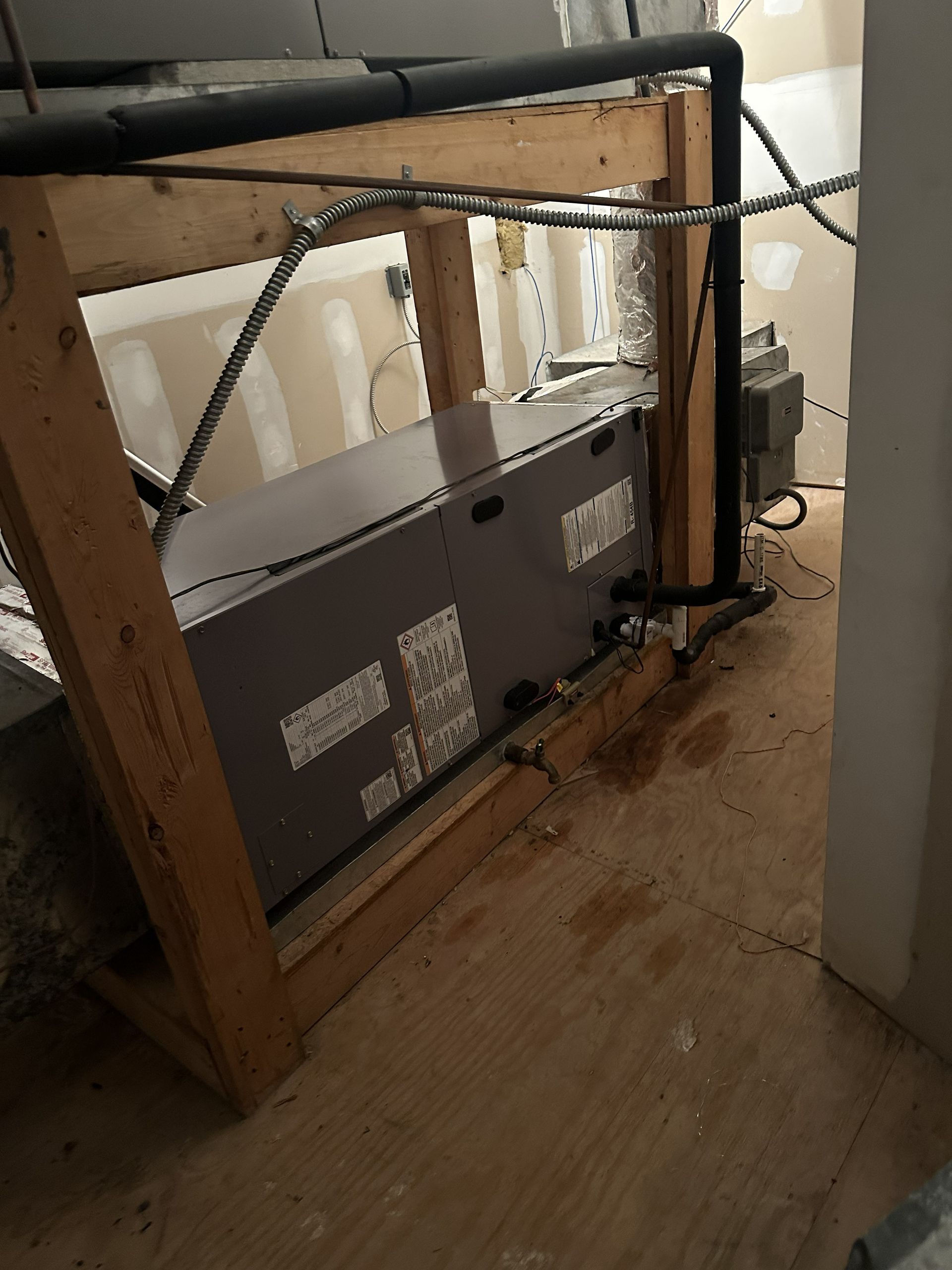 An HVAC air handler unit sits on a wooden frame in a utility closet with visible water stains on the floor below.