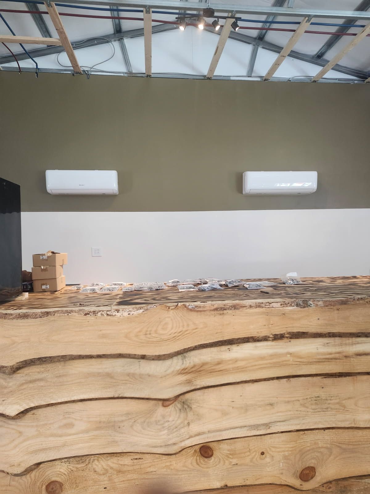 A room under construction with two wall-mounted AC units above a bar made of stacked, unfinished live-edge wood slabs.
