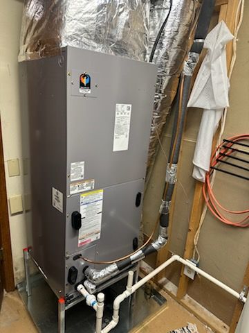 A grey HVAC air handler unit standing on a metal base in a utility closet with connected white PVC and insulated piping.