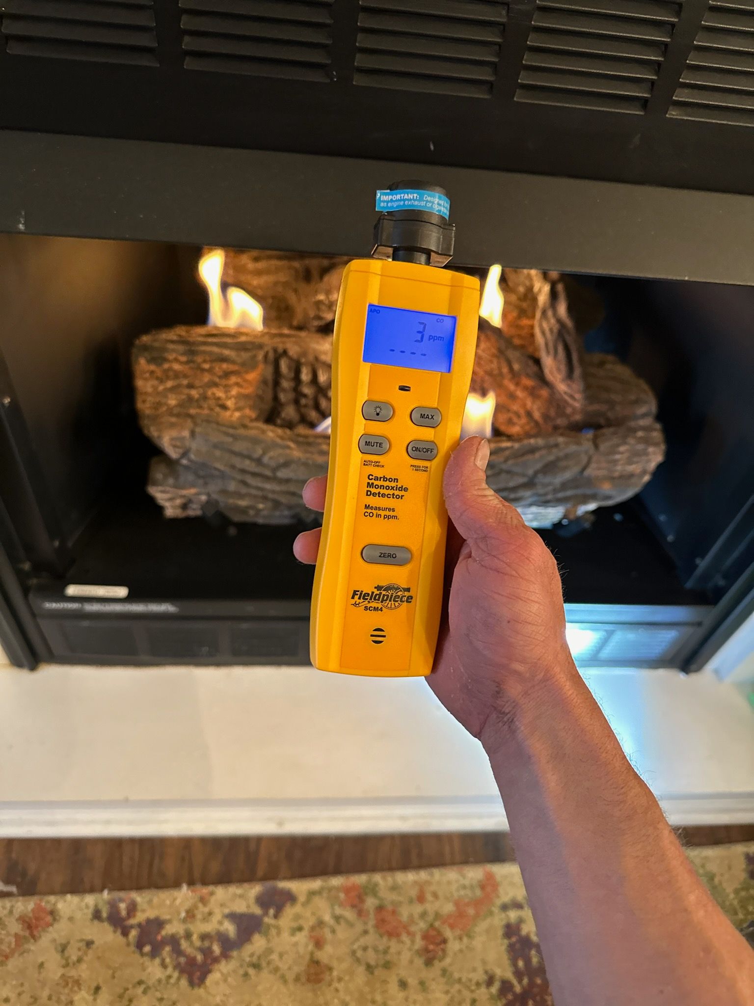 A person holds a yellow gas leak detector in front of a burning fireplace.