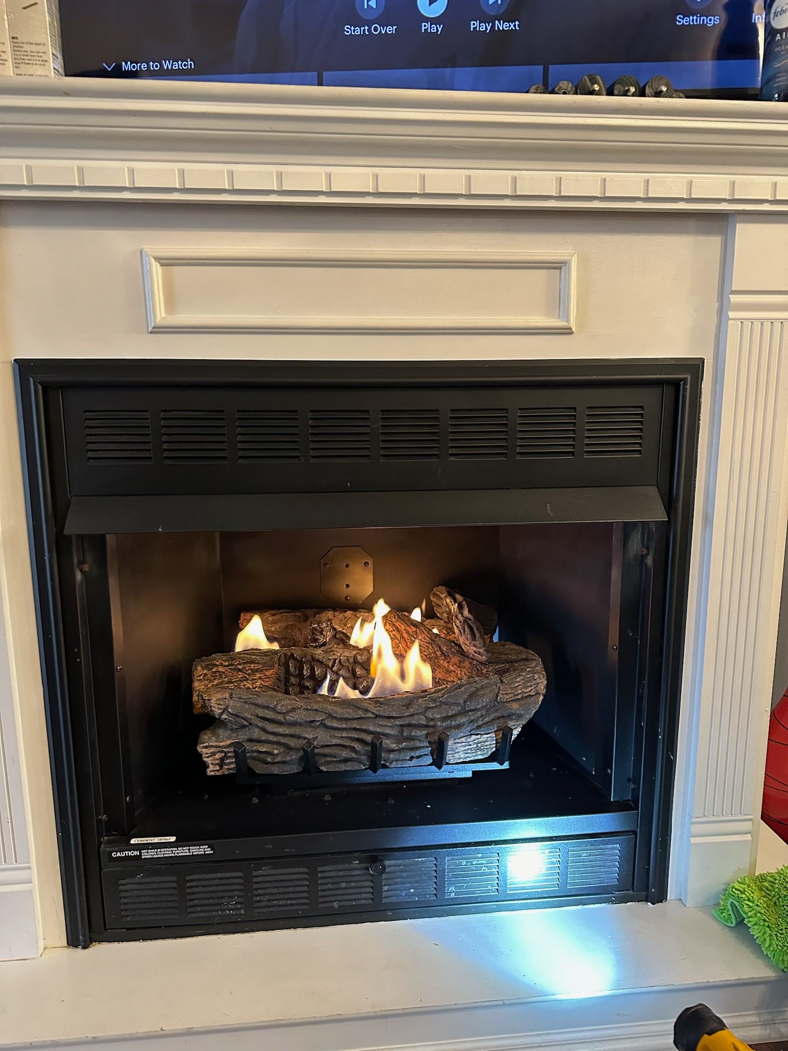 A gas fireplace with a white mantle, black metal frame, and burning logs inside.
