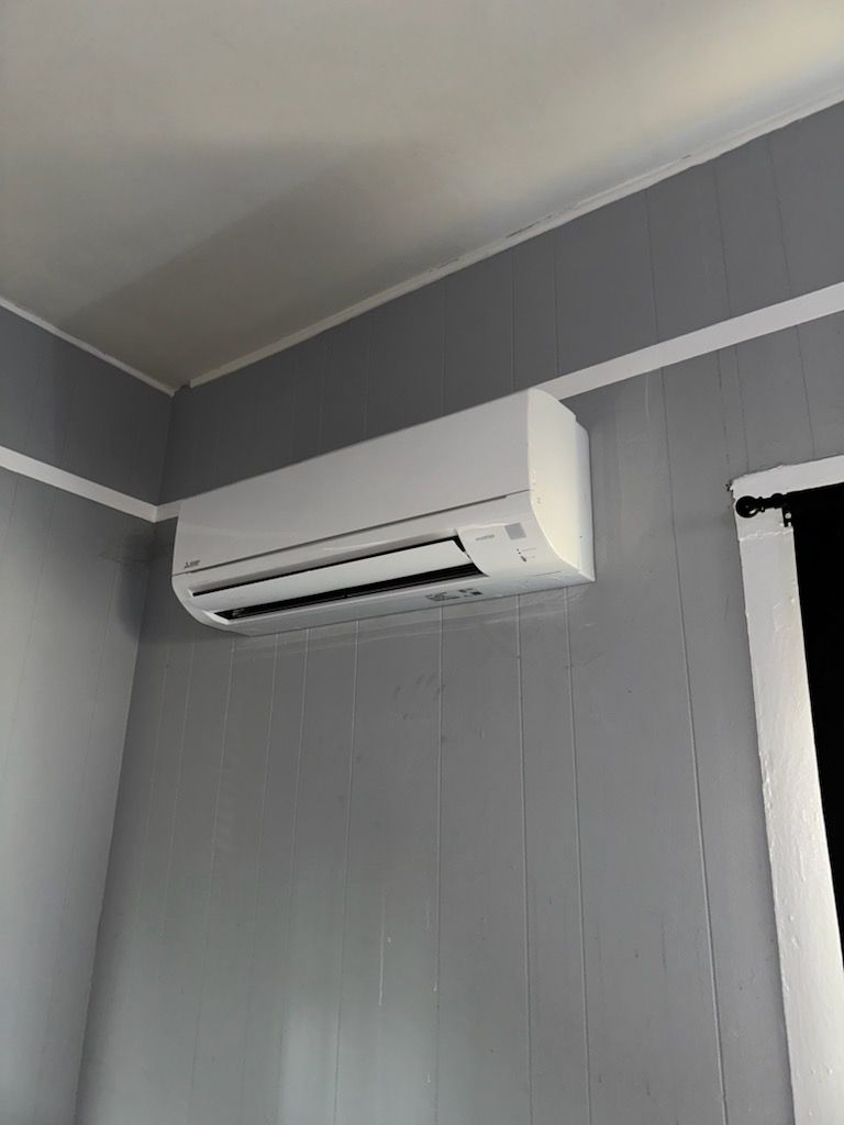 A wall-mounted white air conditioning unit installed high on a grey wall with vertical paneling.