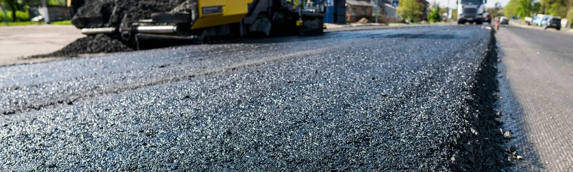 Freshly paved road with a yellow road paver and textured black asphalt in the foreground