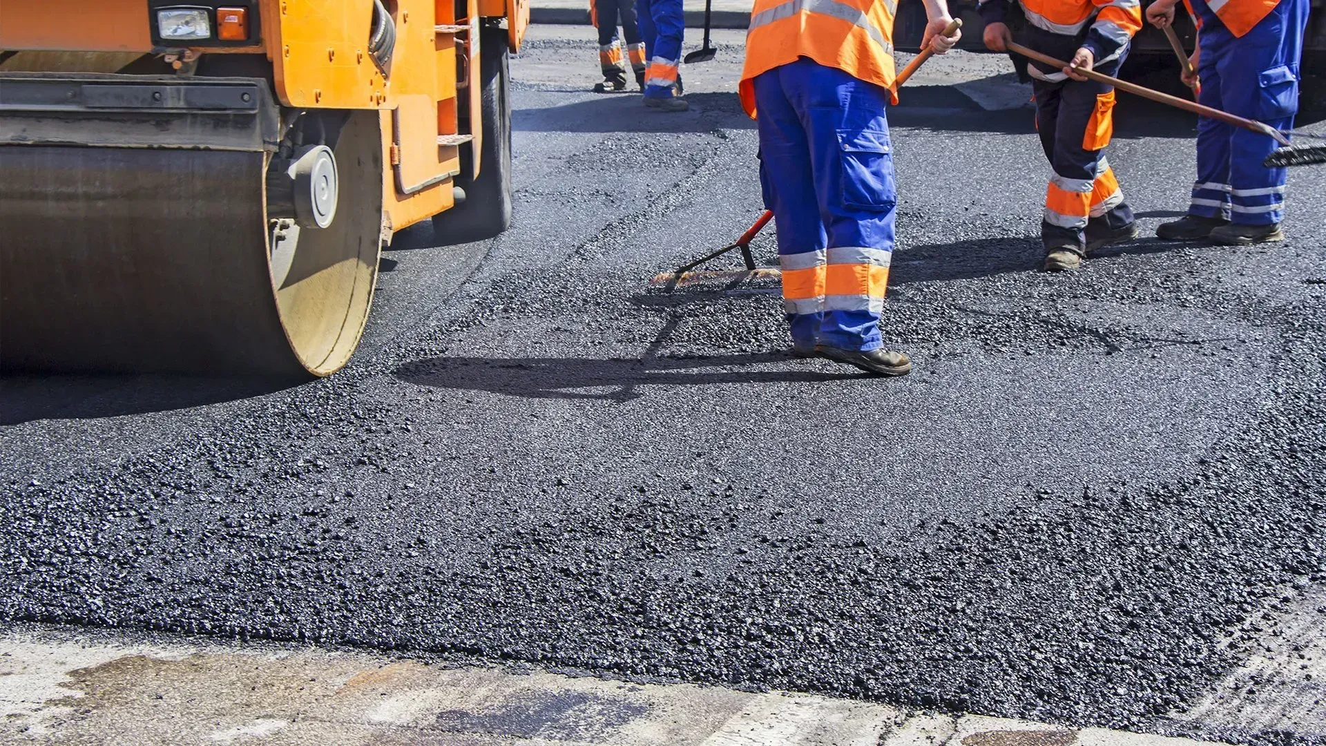 Road crew paving asphalt with a roller and workers in orange safety gear