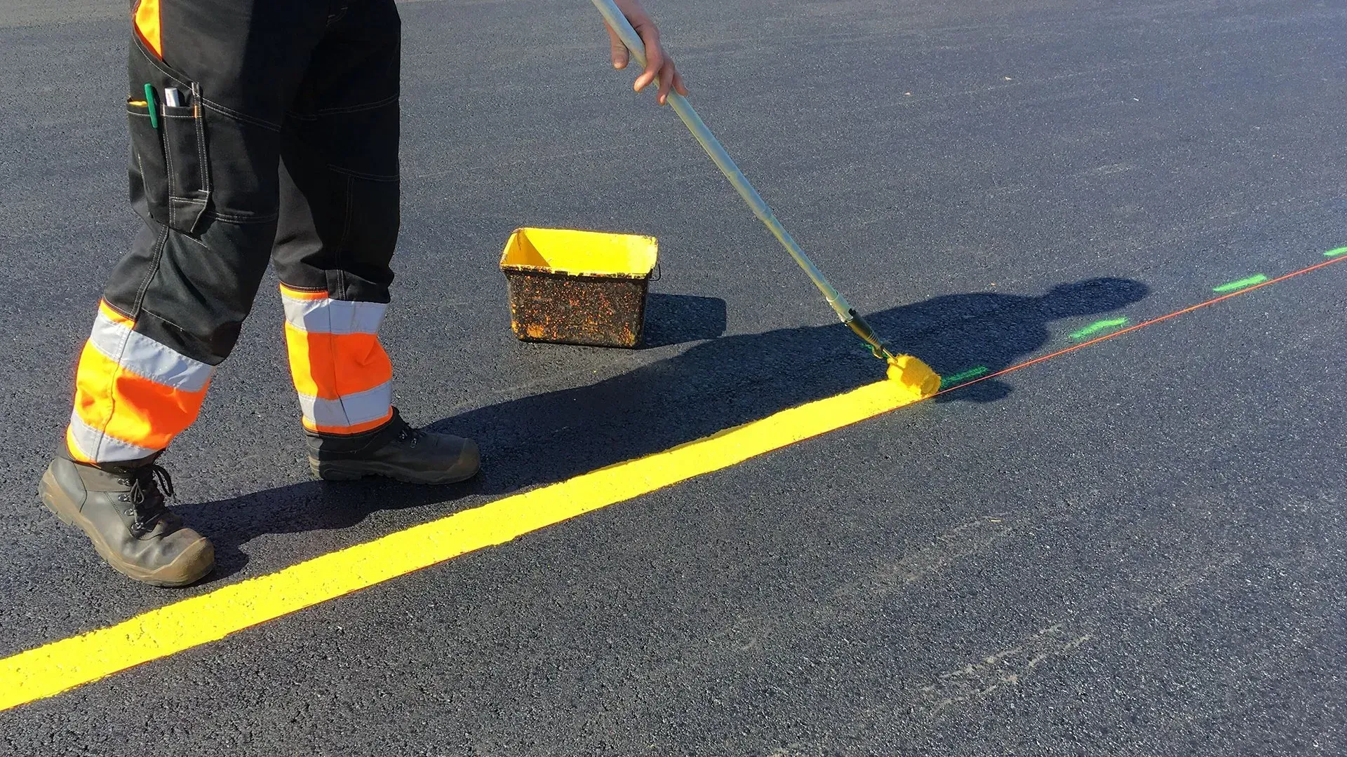 Worker painting a bright yellow road line on asphalt with a roller
