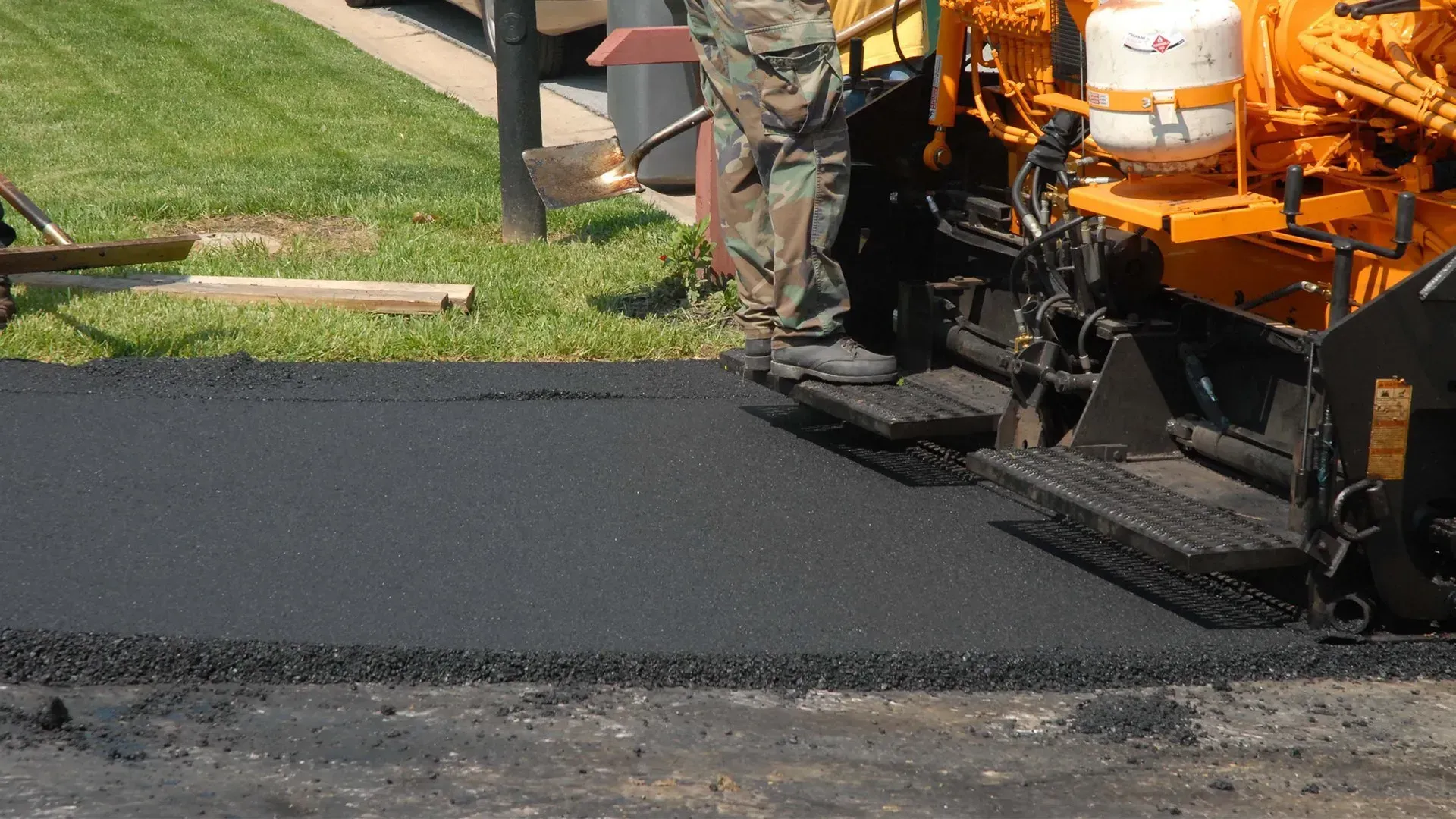 Orange paving machine laying fresh black asphalt on a road.