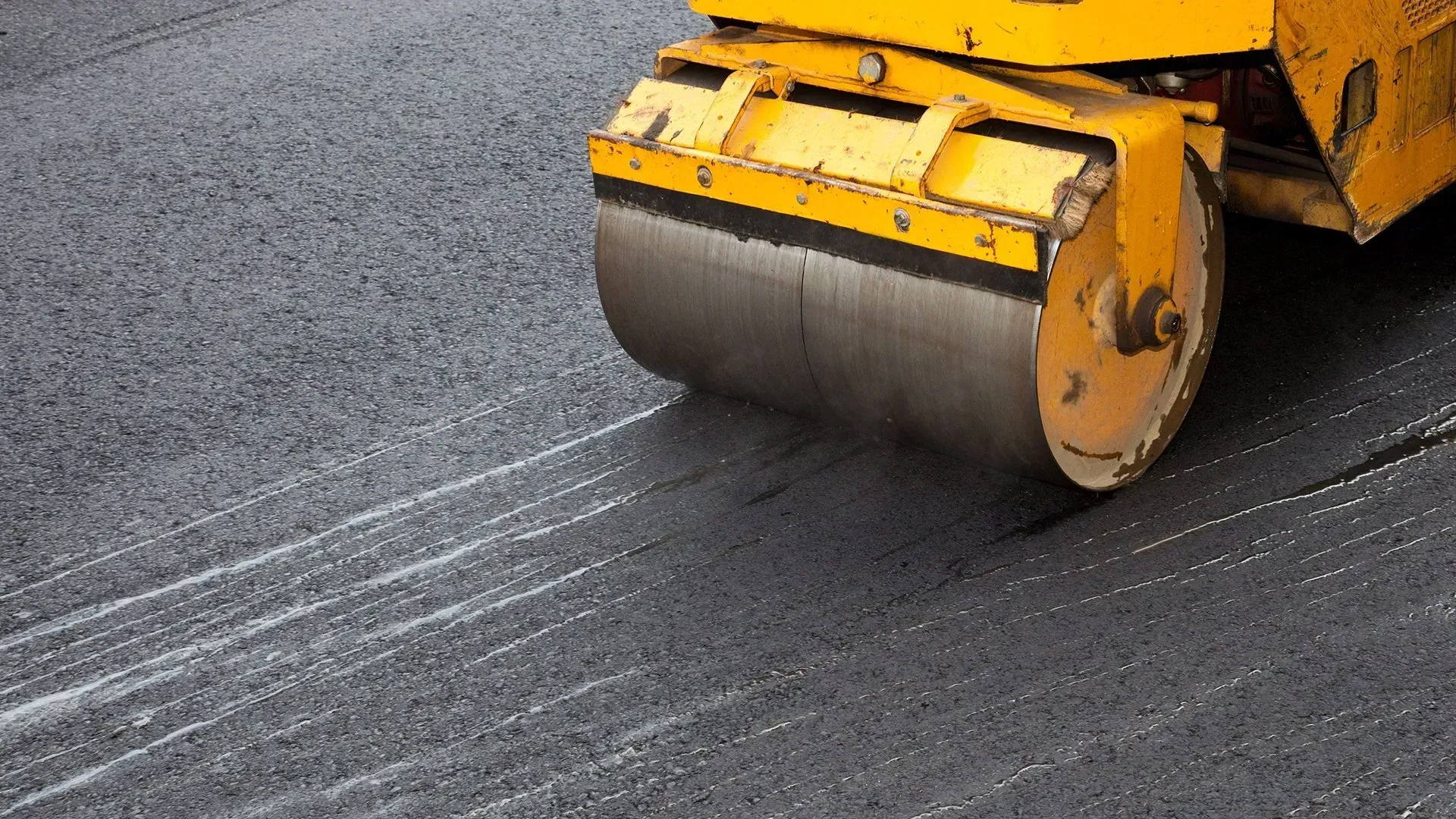 Yellow road roller compacting dark asphalt pavement