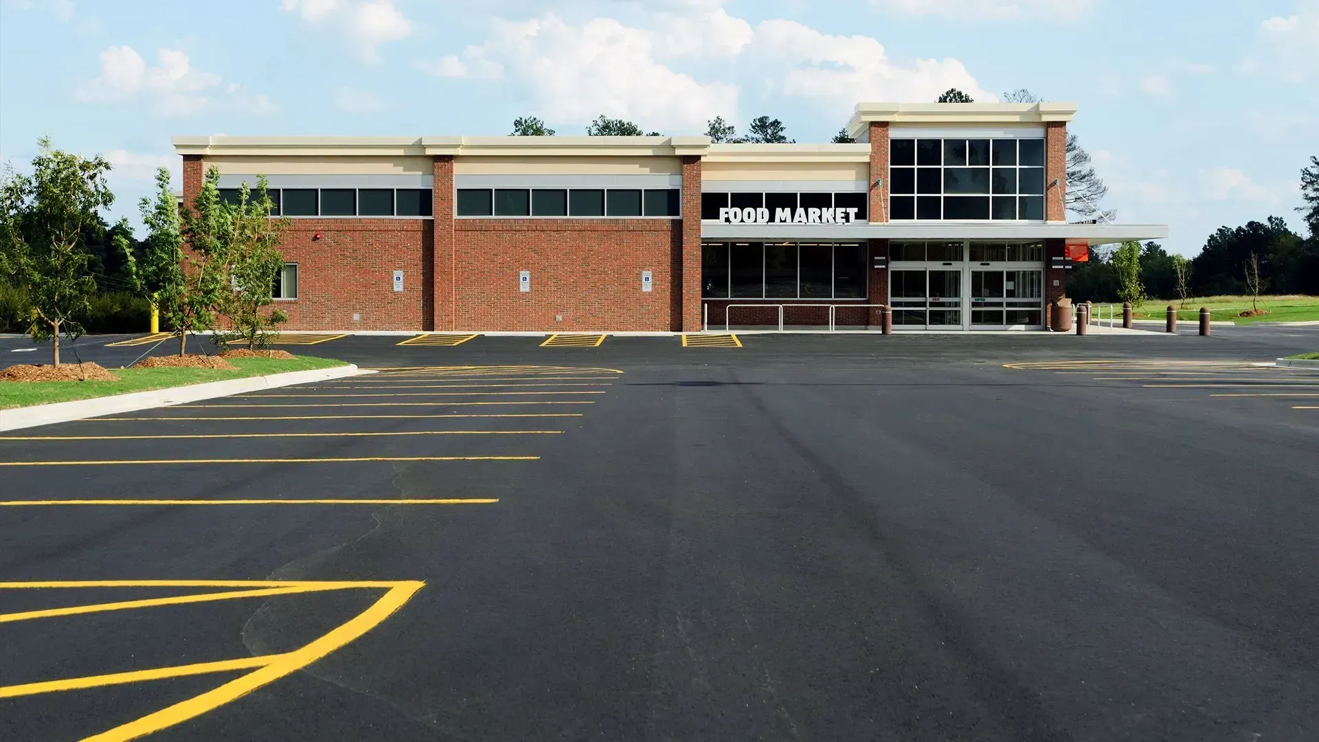 Empty parking lot in front of a red-brick building with large windows under a blue sky