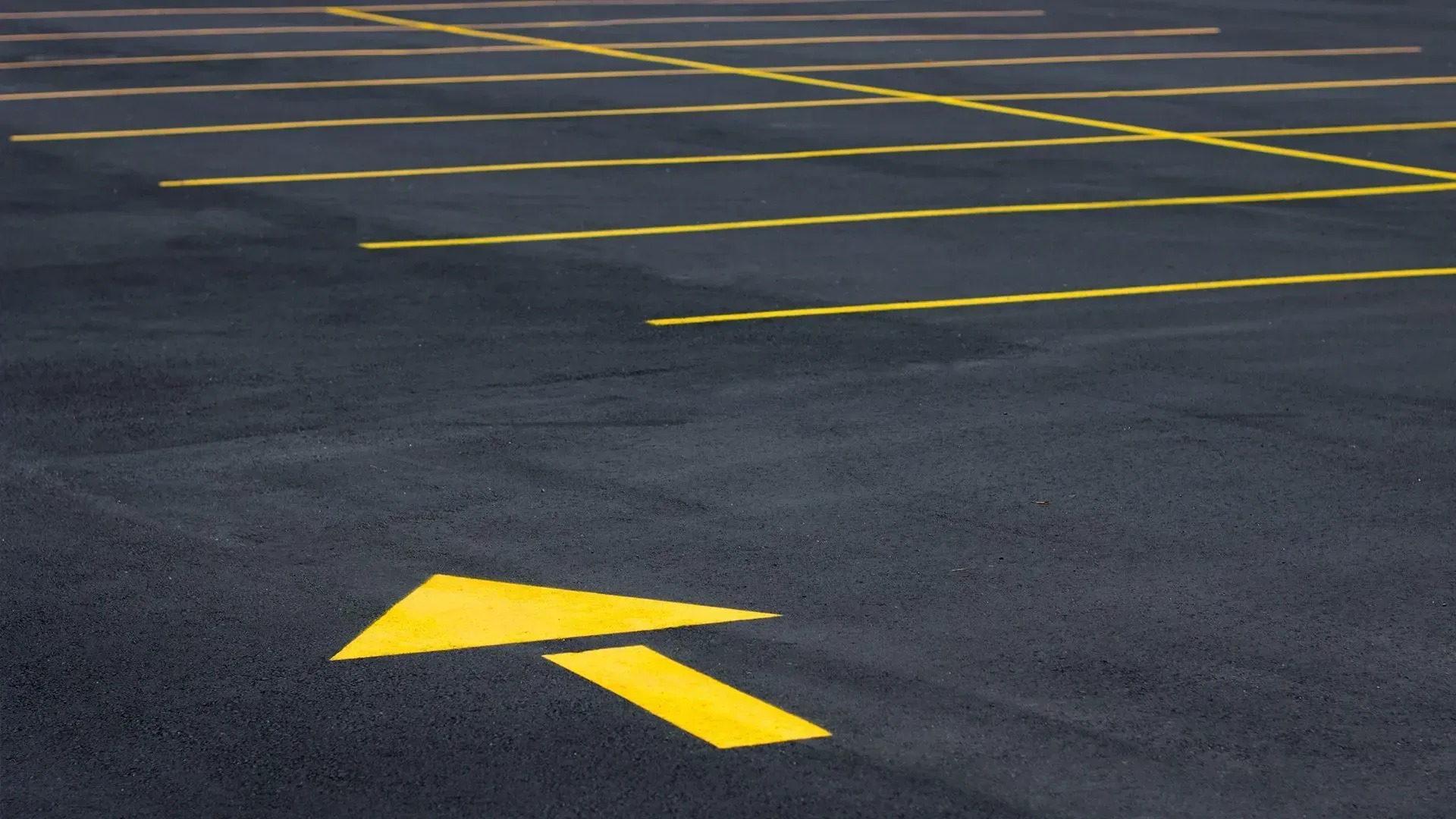 Empty asphalt parking lot with yellow directional arrows and lines painted on the pavement