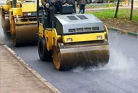 Yellow road roller compacting fresh asphalt on a street