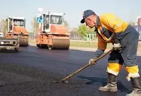 Worker paving asphalt with a rake while two road rollers smooth the surface behind him