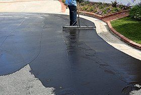Worker spreading black sealant on a driveway with a squeegee