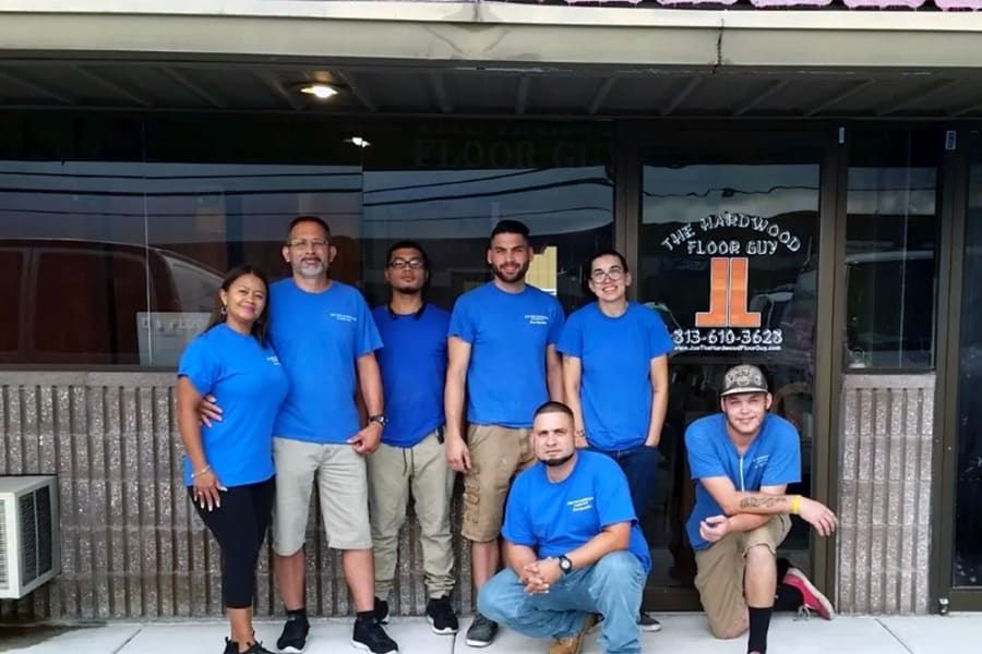Group in blue shirts posing outside a storefront, with one person kneeling in front.