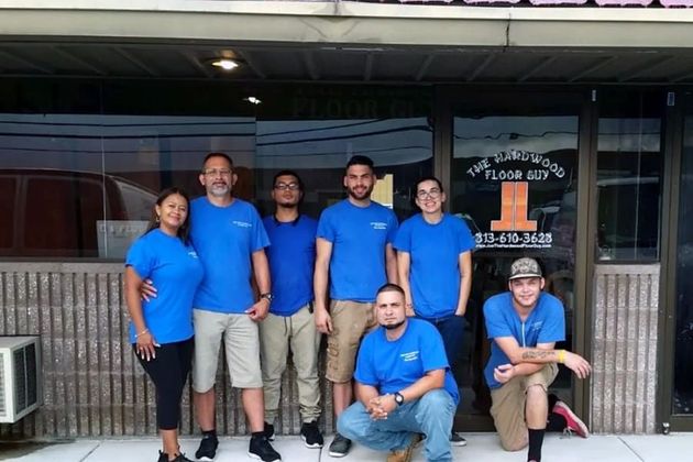 Group in blue shirts posing outside a storefront, with two people seated in front.