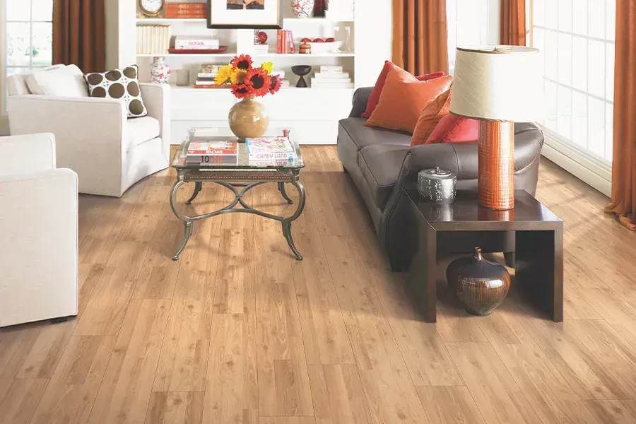 Bright living room with hardwood floors, dark sofa, white chairs, glass coffee table, and orange accents.