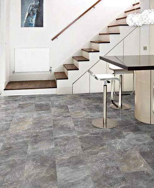 Modern home interior with gray tile floor, staircase, white radiator, and glass dining table with stools