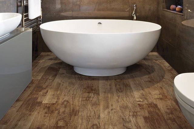Modern bathroom with a large white freestanding bathtub on wood-look flooring.