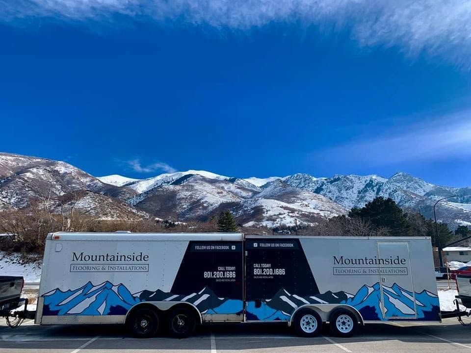 Mountain-side trailer with blue-and-white alpine graphics parked in a snowy landscape beneath mountains.