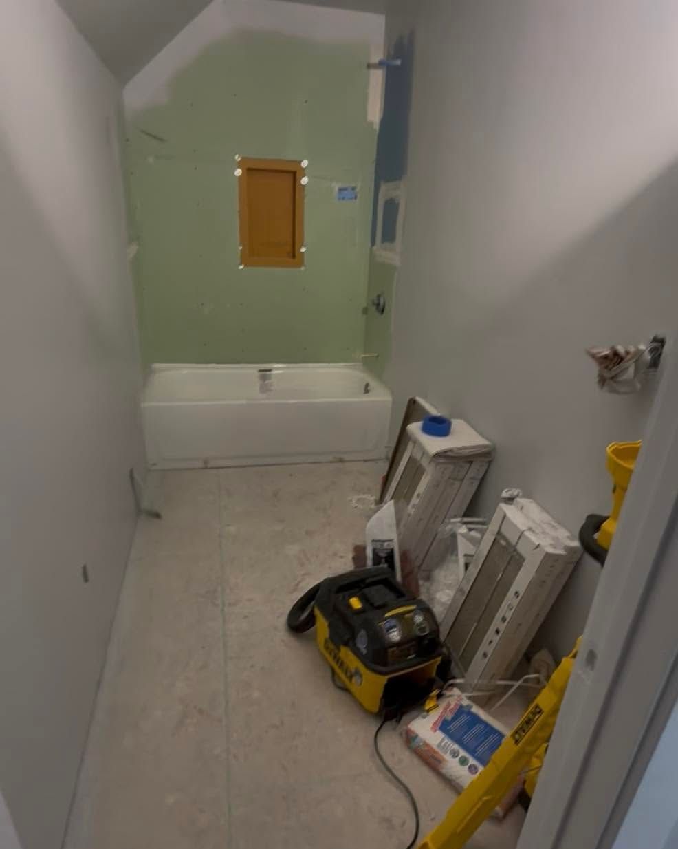 Narrow bathroom under renovation with bathtub, tools, and a yellow vacuum on the floor.
