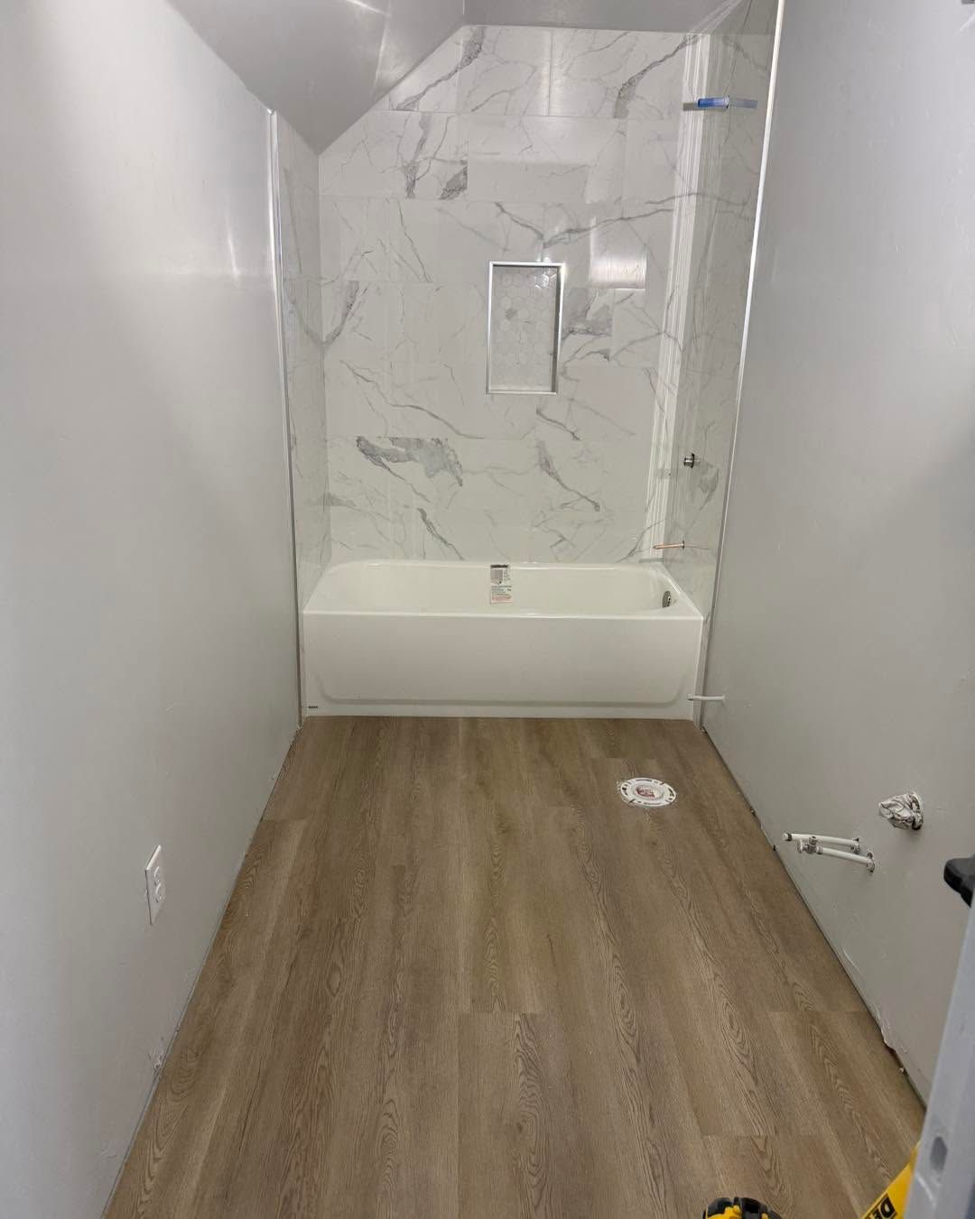 Empty bathroom with wood-look floor, marble shower wall, and white tub alcove