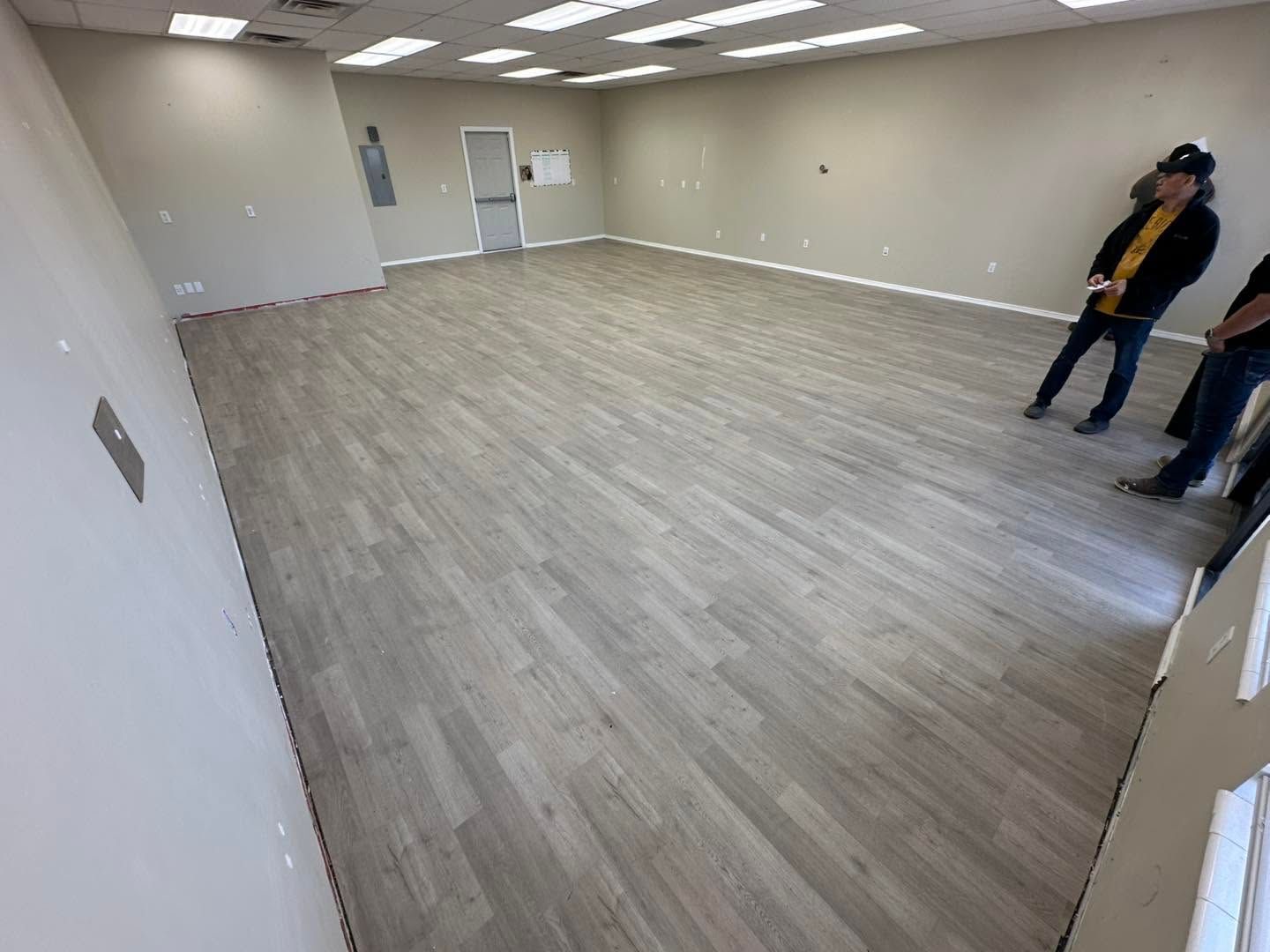 Empty office room with gray flooring and two people standing near the right wall