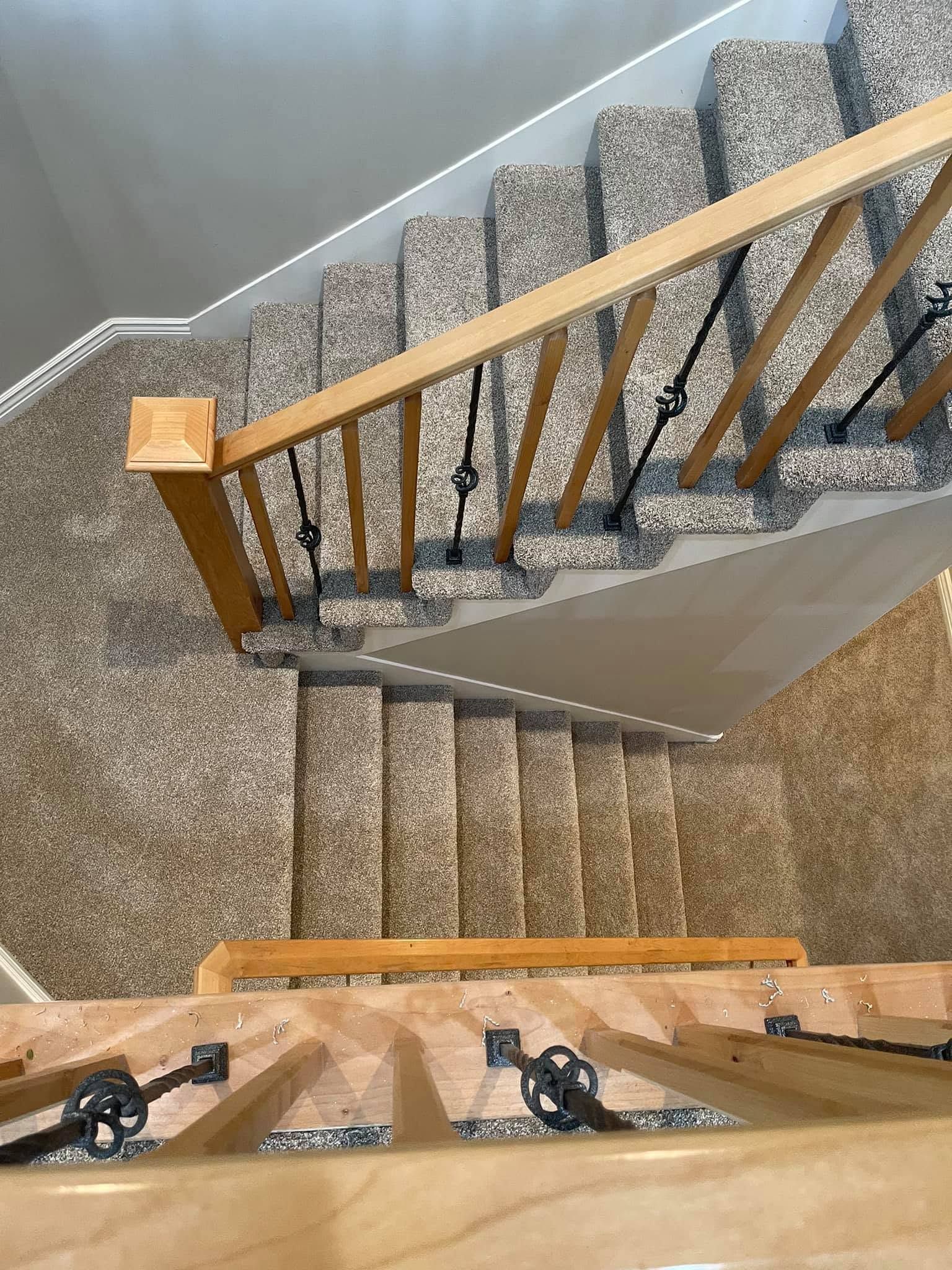 Top-down view of a carpeted staircase with wooden handrails and black balusters.