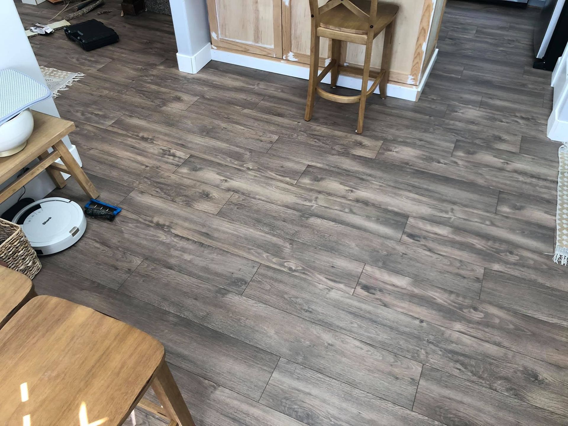 Wood-look flooring in a room with wooden chairs, a cabinet, and a robot vacuum near the wall.