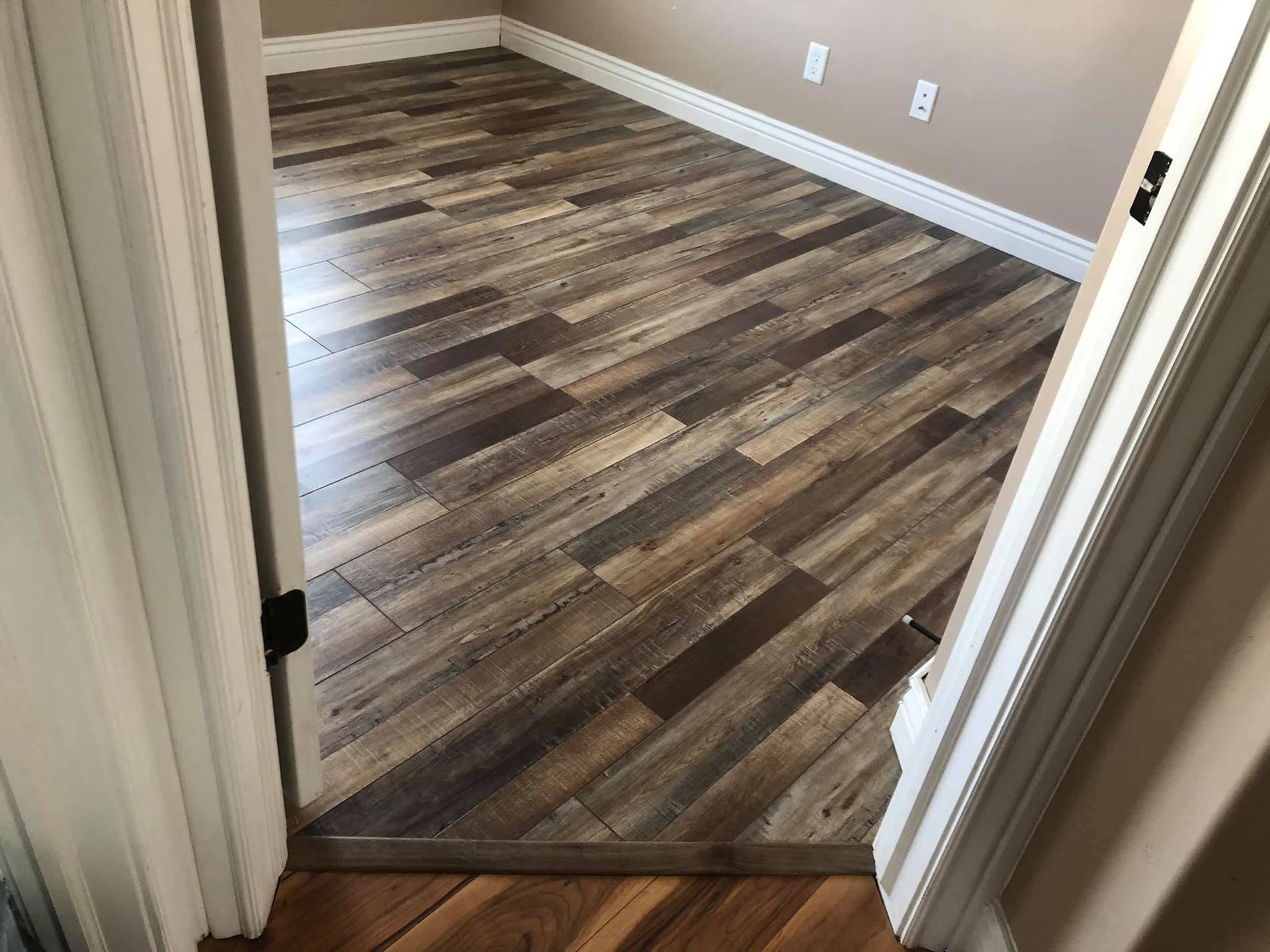 Empty room with wood-look flooring and beige walls, viewed through a doorway.