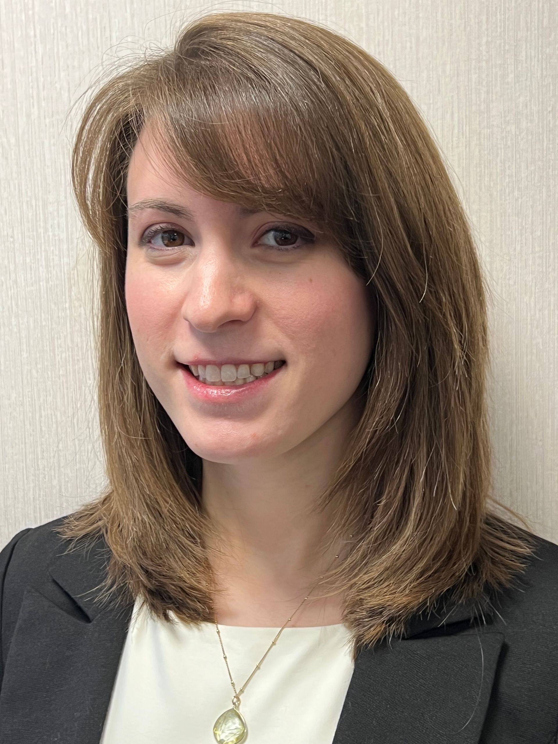 Woman in blazer smiling, light brown hair, wearing a necklace.