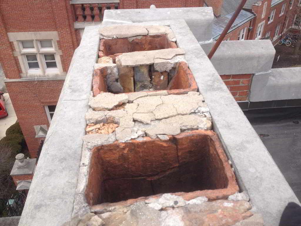 Cracked rooftop masonry with several rectangular openings above a brick building