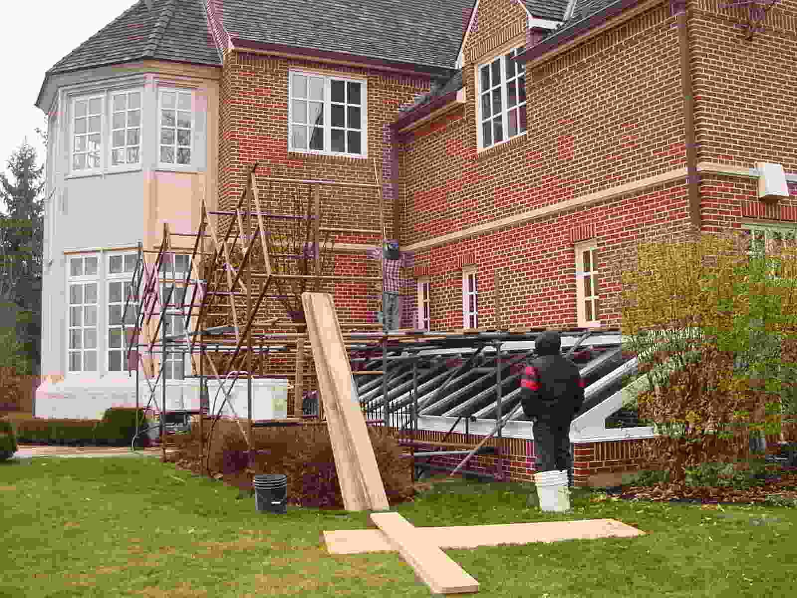 Workers setting up scaffolding and a ramp beside a brick house under renovation