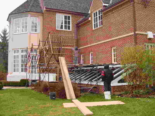 House exterior with scaffolding and workers installing long wooden boards by the wall