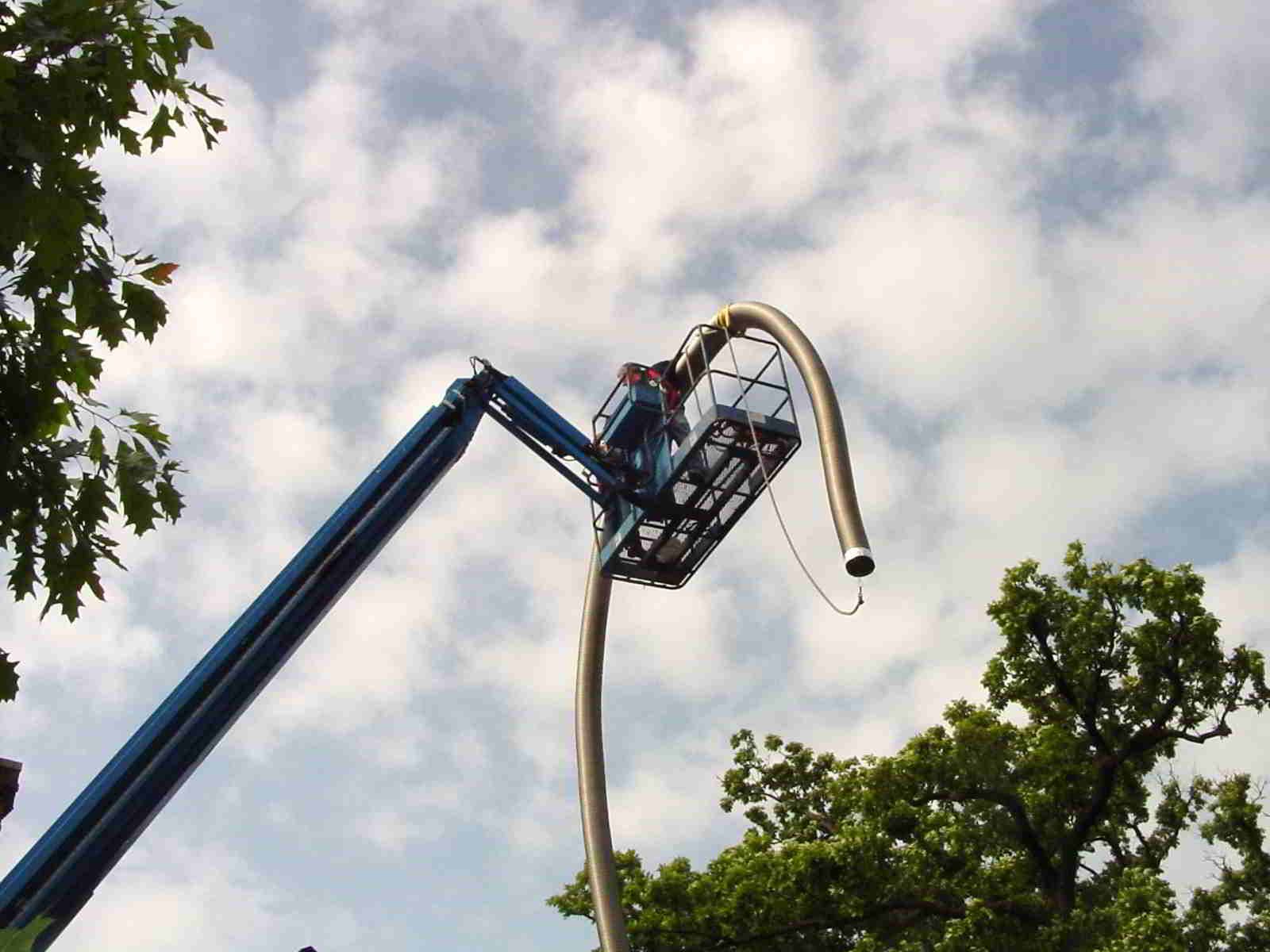 Blue boom lift with a worker raised high among trees against a cloudy sky