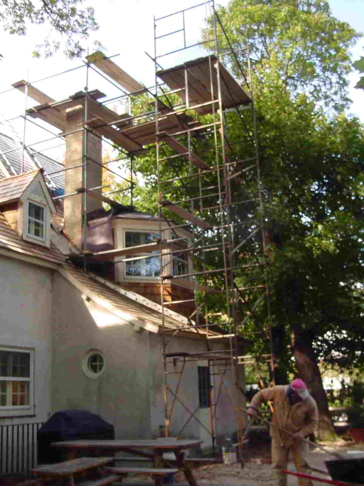 Scaffolding around a house with a tree beside it and a person working near the bottom