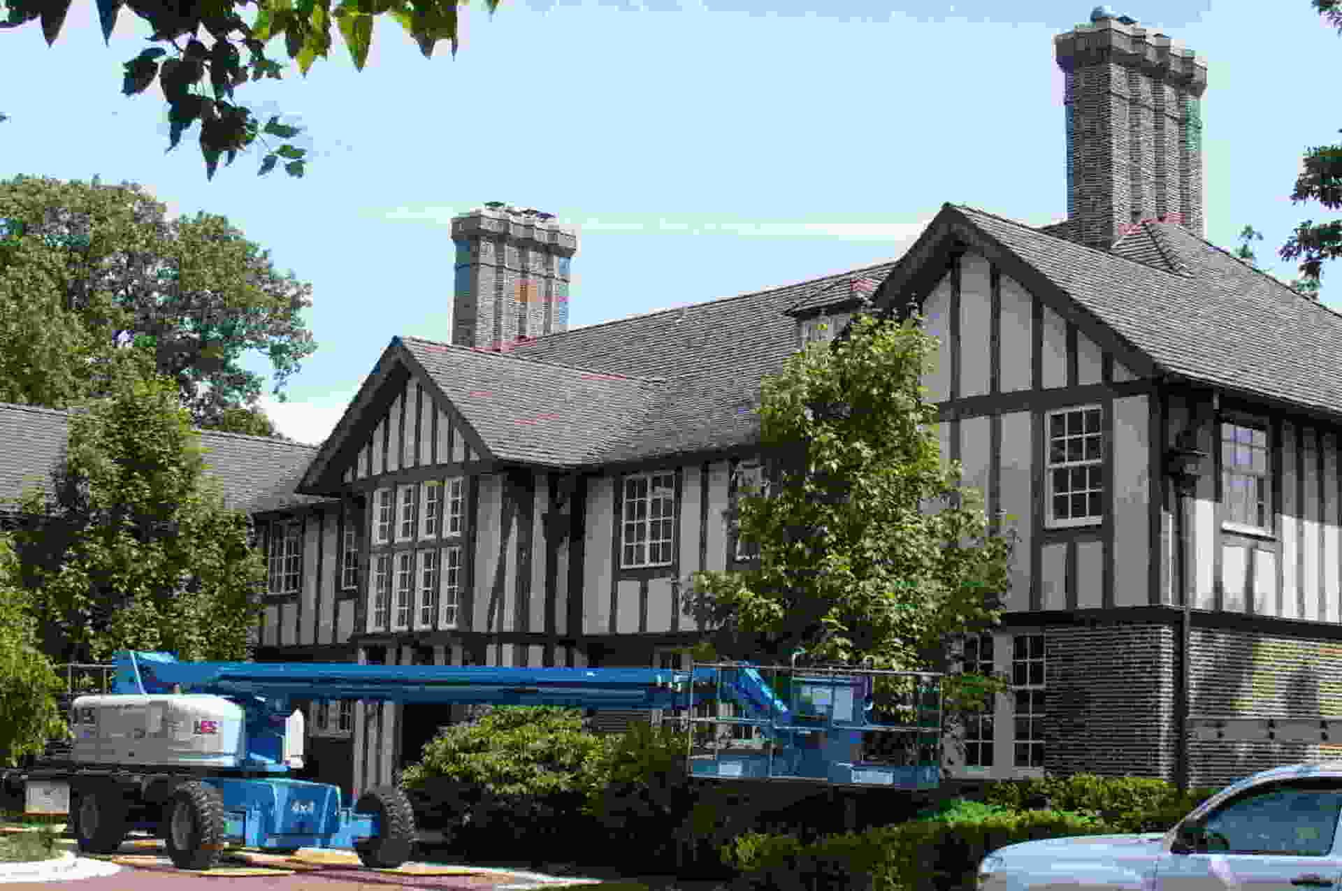 Tudor-style building with blue utility lift and parked cars in front, under a clear sky