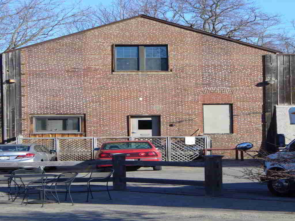 Brick building with parked cars in front and a fence, seen in daylight.